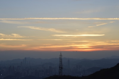 A panoramic view of a city skyline with telecommunications towers at sunset.