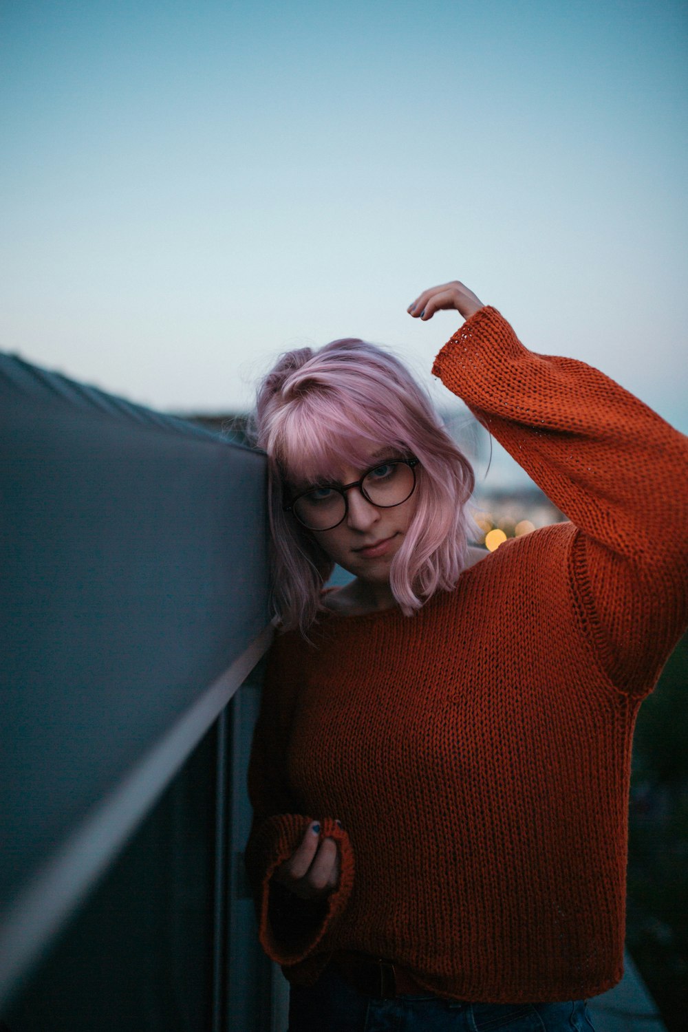 Femme en pull rouge appuyée sur un mur de béton gris