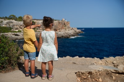 two children standing near cliff watching on ocean at daytime visionary zoom background