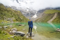 woman standing in front of body of water and mountain