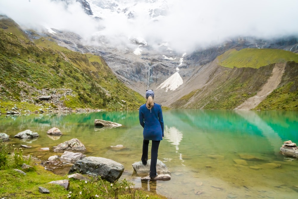 woman standing in front of body of water and mountain