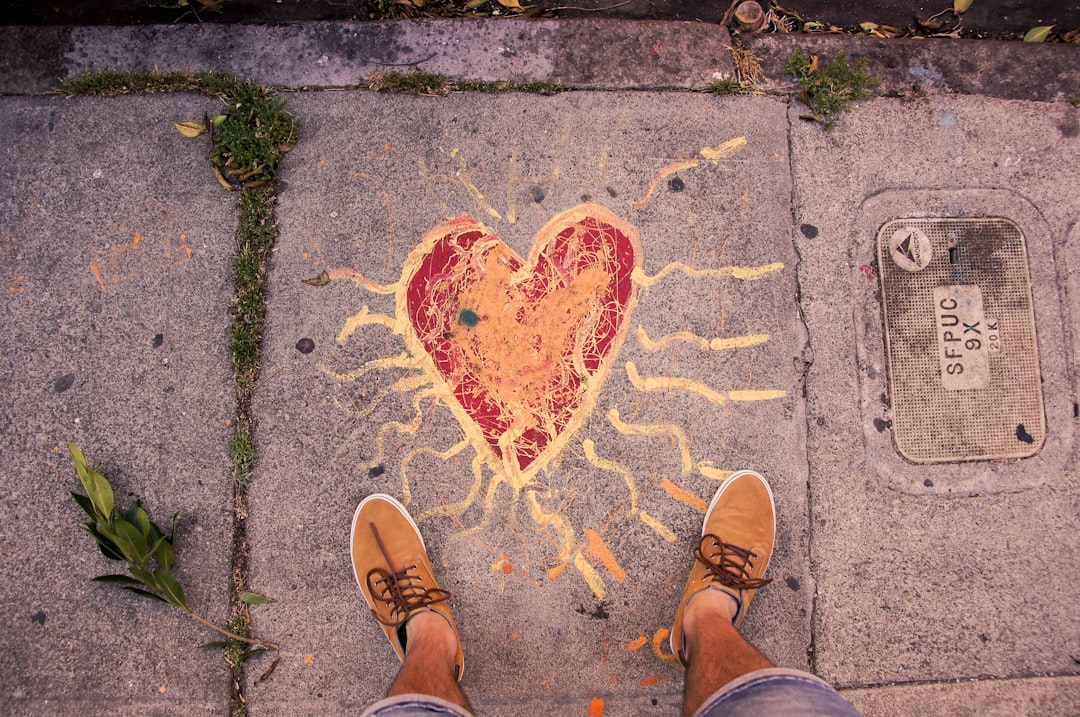 Photo of chalk heart with rays extending outwards. Person's feet standing while taking the photo.