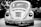 A vintage car with a classic design is parked outdoors, prominently displaying a license plate with the numbers 4473 SJ 21. The car is captured in grayscale, highlighting its distinctive round tail lights and the intricate detailing on the rear vent and bumper.