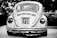 A vintage car with a classic design is parked outdoors, prominently displaying a license plate with the numbers 4473 SJ 21. The car is captured in grayscale, highlighting its distinctive round tail lights and the intricate detailing on the rear vent and bumper.