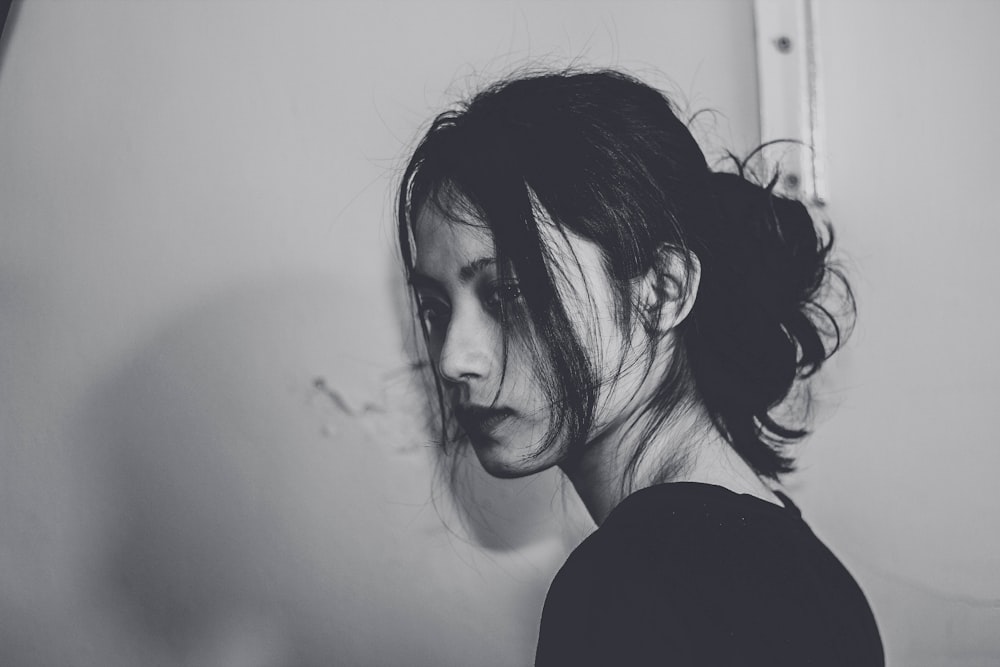 grayscale photography of woman standing near wall