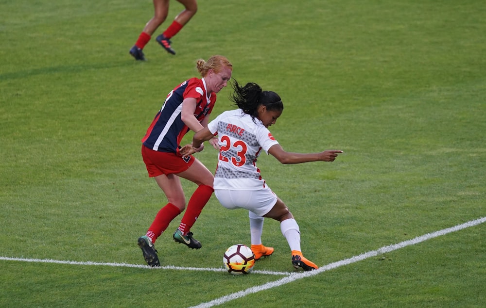 two women playing soccer on field