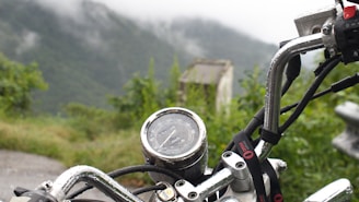 Close-up of a rider's hand gripping the handlebar with lush green mountains in the background.
