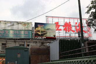 Billboards and signs in an outdoor setting display both English and Chinese text. The prominent sign advertises the Sea King Garden Restaurant, while another sign features an image of a restaurant by water at night.