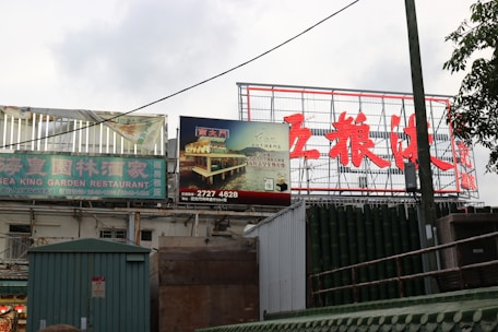 Billboards and signs in an outdoor setting display both English and Chinese text. The prominent sign advertises the Sea King Garden Restaurant, while another sign features an image of a restaurant by water at night.
