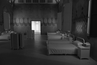 A room with multiple neatly arranged white beds, each paired with a small side table, creating a sense of symmetry. The walls feature geometric patterns, and there is a radiator placed near the doorway, which is illuminated from another room.