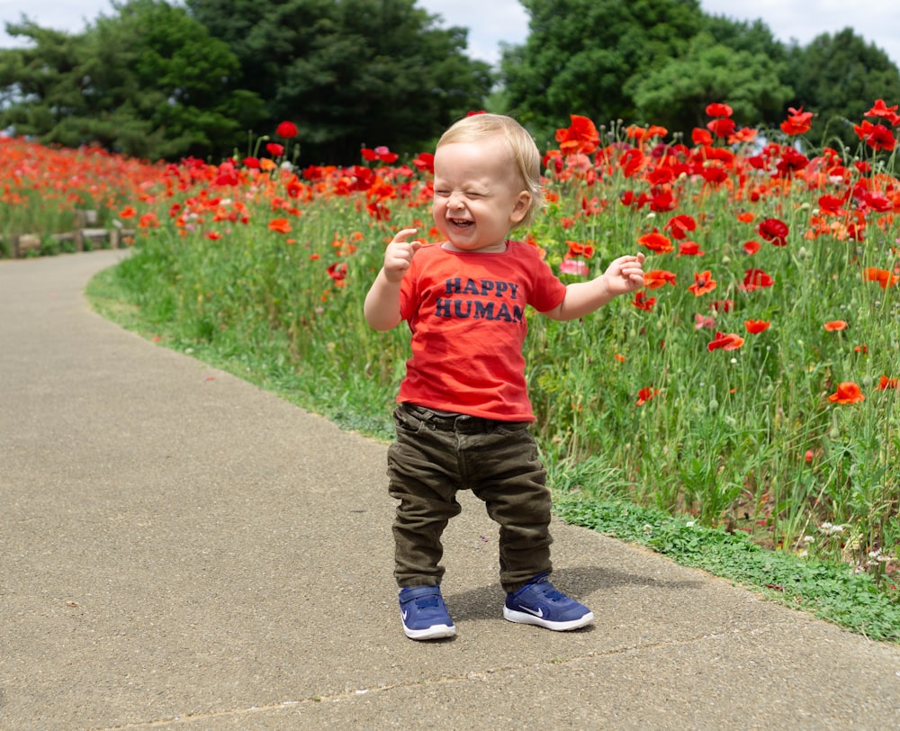 toddler laughing while standing near red petaled flowers