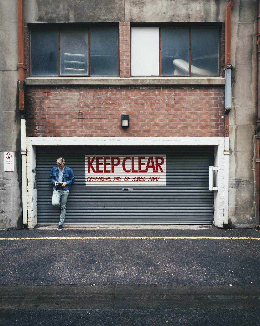 man wearing blue denim jacket while leaning against roller shutter