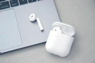 Close-up of a wireless earbud case open on a clean white desk.