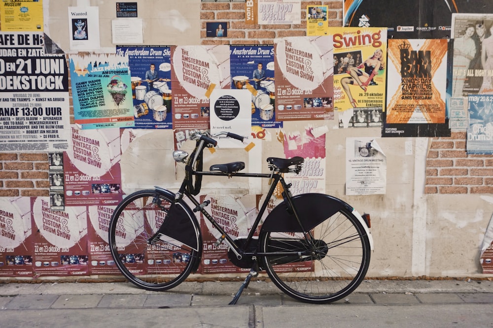 black bicycle parked beside a wall full of poster