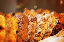 A close-up view of a row of freshly baked cookies, dusted with powdered sugar. The cookies appear golden brown and textured, suggesting they might contain chocolate chips or nuts.
