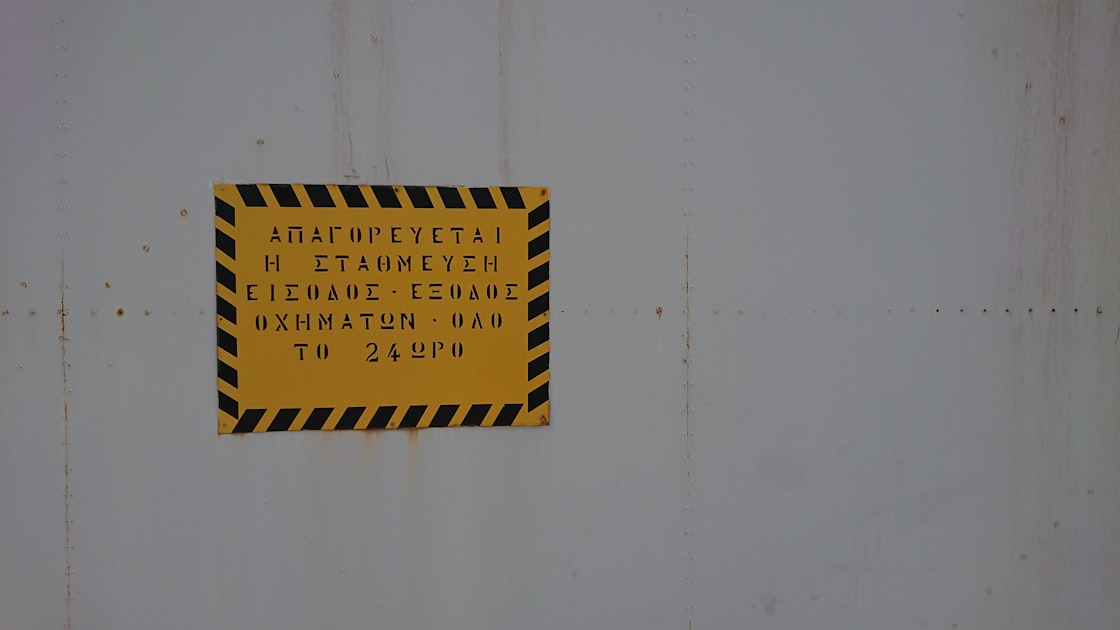 Placa de aviso amarela e preta em parede industrial
