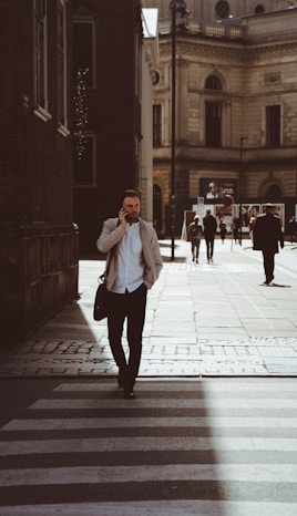 man holding phone while standing on pedestrian lane