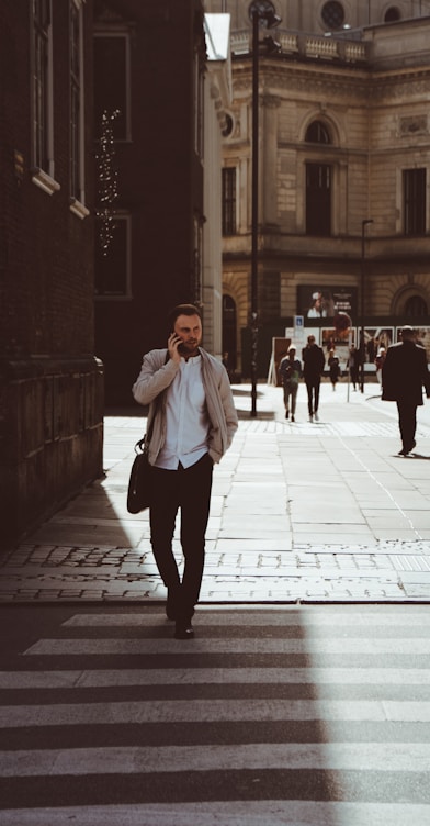 man holding phone while standing on pedestrian lane