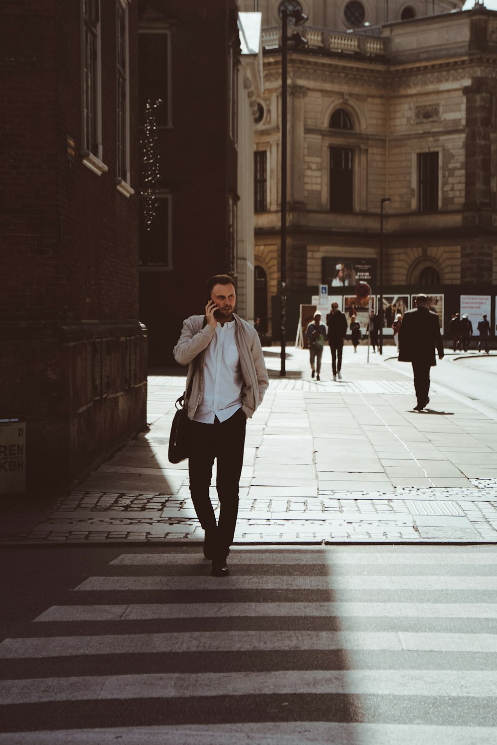 man holding phone while standing on pedestrian lane