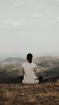 woman sitting on cliff overlooking mountains during daytime