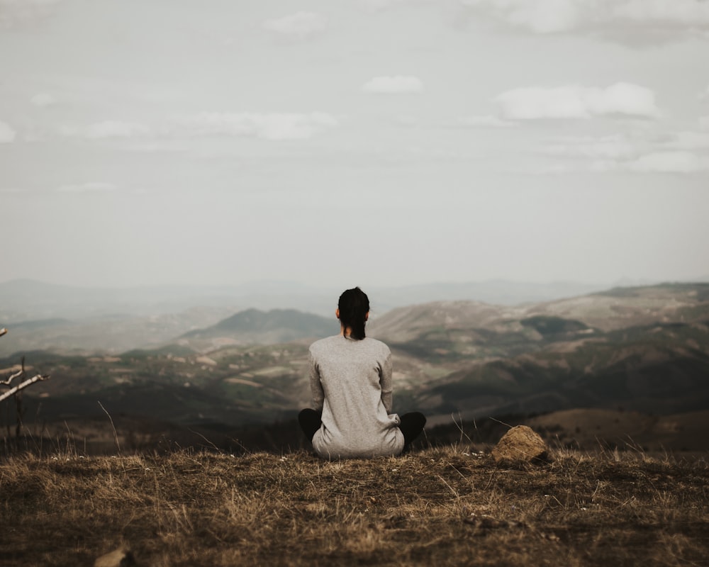 woman sitting on cliff overlooking mountains during daytime