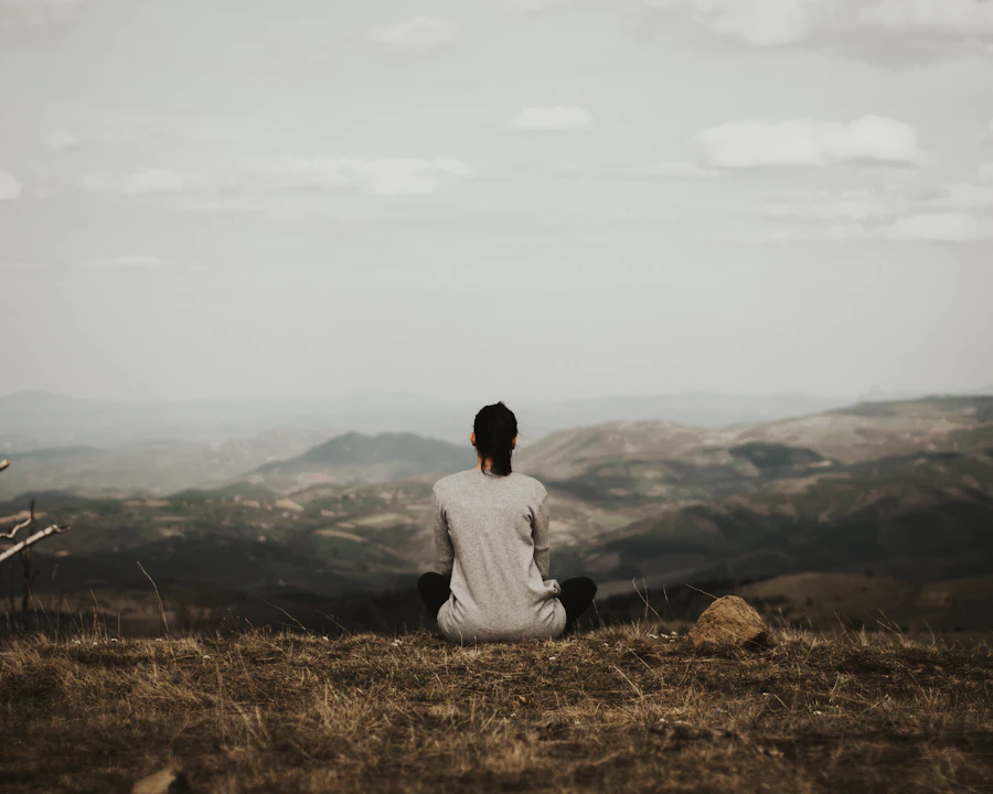 Person sitzt still meditierend mit Blick auf Berge, von hinten fotografiert