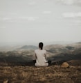 woman sitting on cliff overlooking mountains during daytime