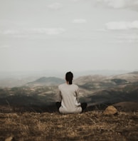 woman sitting on cliff overlooking mountains during daytime