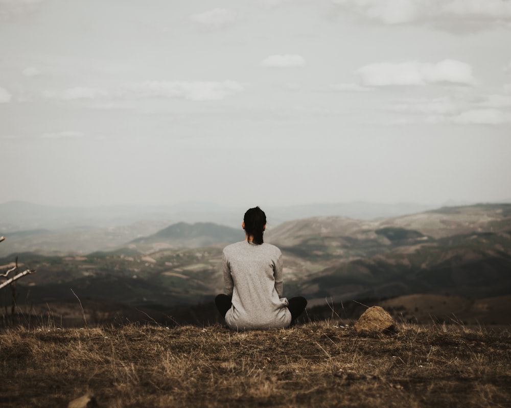 mulher sentada no penhasco com vista para as montanhas durante o dia