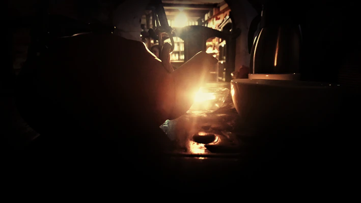 A dark romantic candlelit table setting featuring a ceramic mug with steam rising gently.