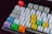 A mechanical keyboard with a variety of colorful keycaps, including red, blue, green, yellow, and purple. The keys contain a mix of English letters, symbols, and playful icons. The background is dark, making the colors of the keys stand out vividly.