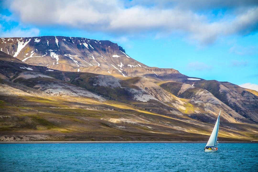 sailing boat on ocean with snow-capped mountain at distance