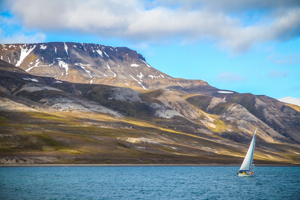 sailing boat on ocean with snow-capped mountain at distance