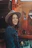 Smiling woman wearing a hat standing beside a rugged 4x4 vehicle on a dusty trail.