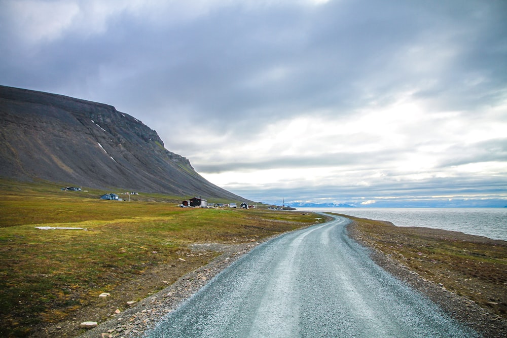 winding road near mountain range and body of water under nimbus clouds