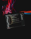 A computer screen displaying code is set against a dark background with dynamic streaks of red and blue light. The code appears to be in a text editor or IDE, with a clear folder structure on the left and lines of syntax-highlighted text taking up the central portion. The colorful light streaks add a sense of motion and energy.