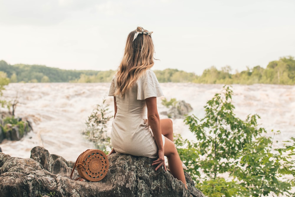 woman sitting on rock beside body of water