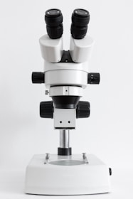 A laboratory microscope with dual eyepieces and several adjustment knobs on a sturdy base, designed for precision and close examination of small objects.
