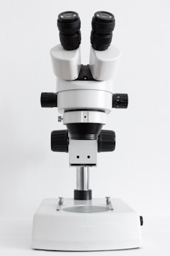 A laboratory microscope with dual eyepieces and several adjustment knobs on a sturdy base, designed for precision and close examination of small objects.
