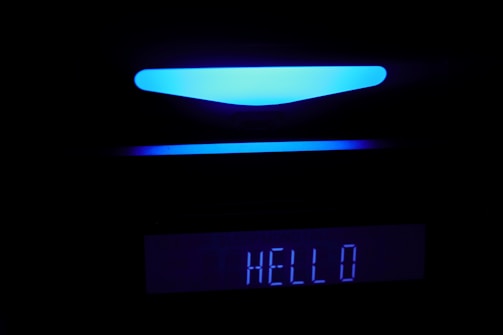 A black background showcases a digital display with a glowing blue light above a rectangular screen that reads 'HELLO' in bright letters.