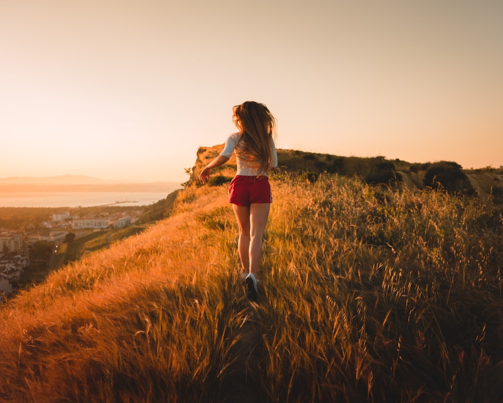 femme courant dans le champ d’herbe au coucher du soleil