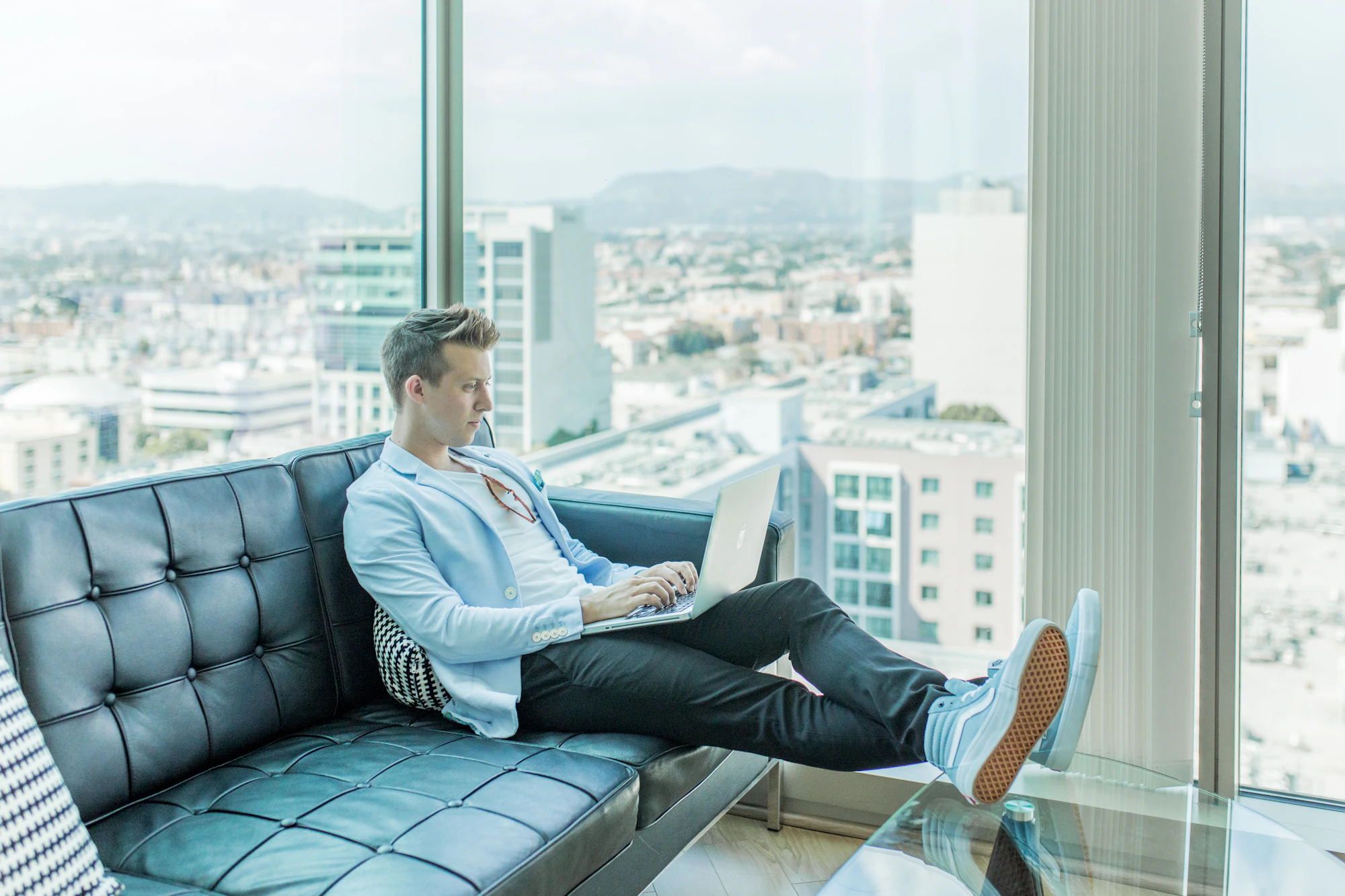 Ikamet client, a digital nomad, on a black sofa in a high-rise with floor-to-ceiling windows.
