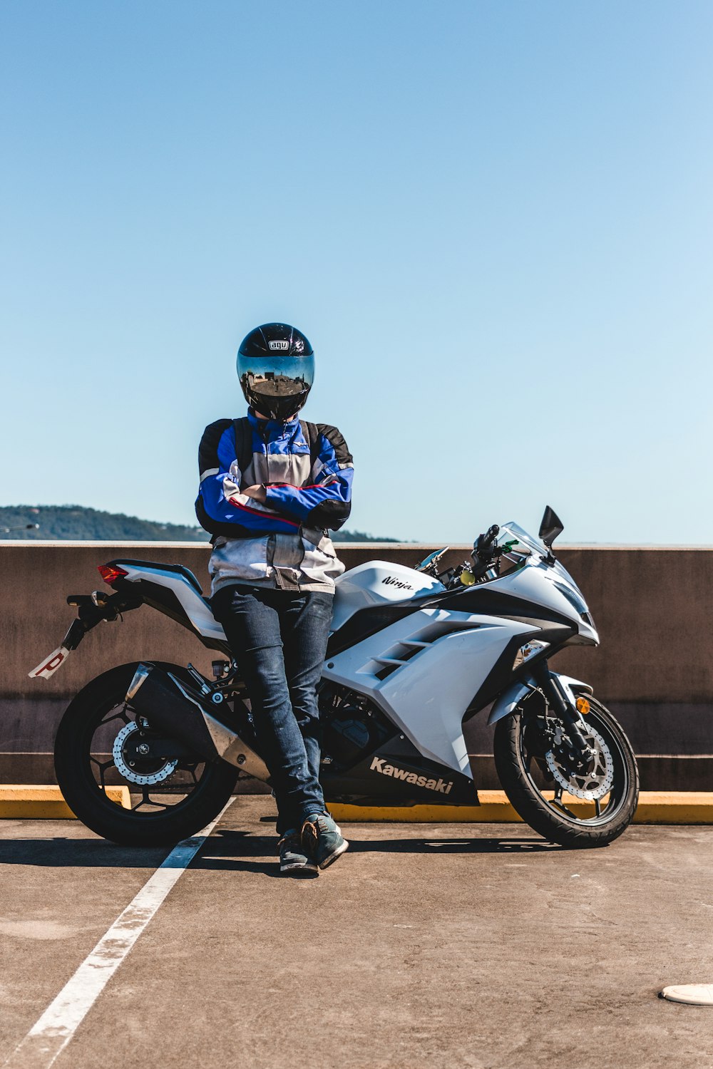person wearing helmet standing and leaning on Kawasaki sports bike during daytime