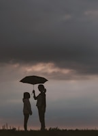 silhouette of woman holding umbrella standing in front of girl on hill during night time