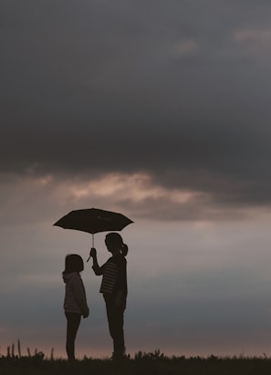 silhouette of woman holding umbrella standing in front of girl on hill during night time