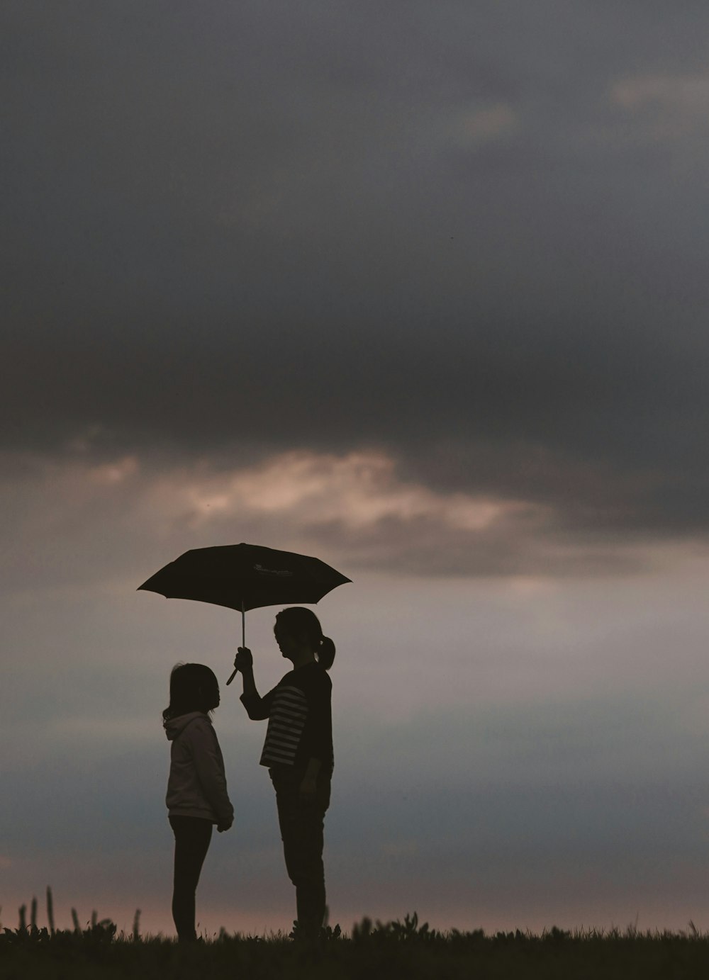 밤 시간 동안 언덕에 소녀 앞에 서 있는 우산을 들고 있는 여자의 실루엣