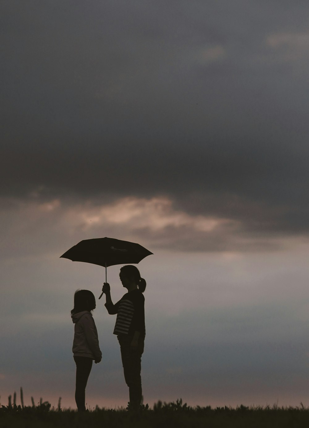 silhouette of woman holding umbrella standing in front of girl on hill during night time