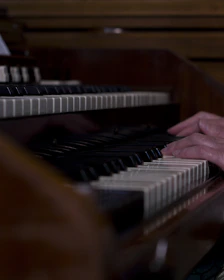 A close-up of hands playing gospel piano keys in a warmly lit church setting.