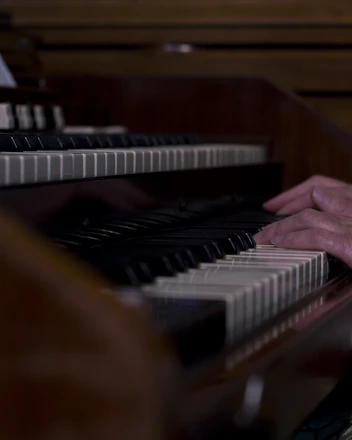 Close-up of a musician’s hands playing a piano keyboard under soft spotlight.