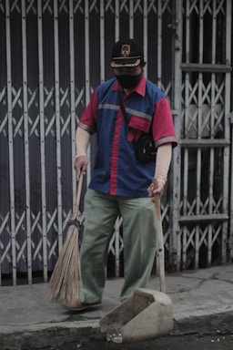 A friendly cleaner in uniform holding cleaning supplies outside a cozy home.